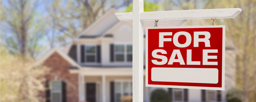 A close up view of a "for sale" sign in front of a house